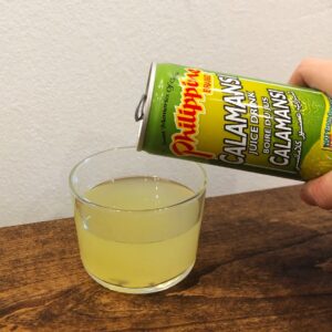 Calamansi Juice Drink being poured into a small glass on a wooden surface