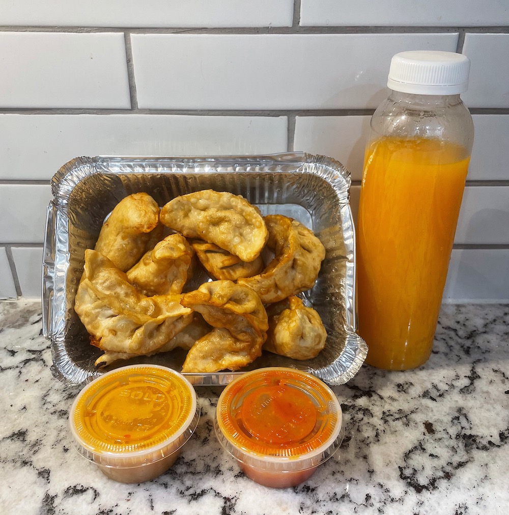 Container of fried momos with sauces and fresh orange juice from Too Good To Go App