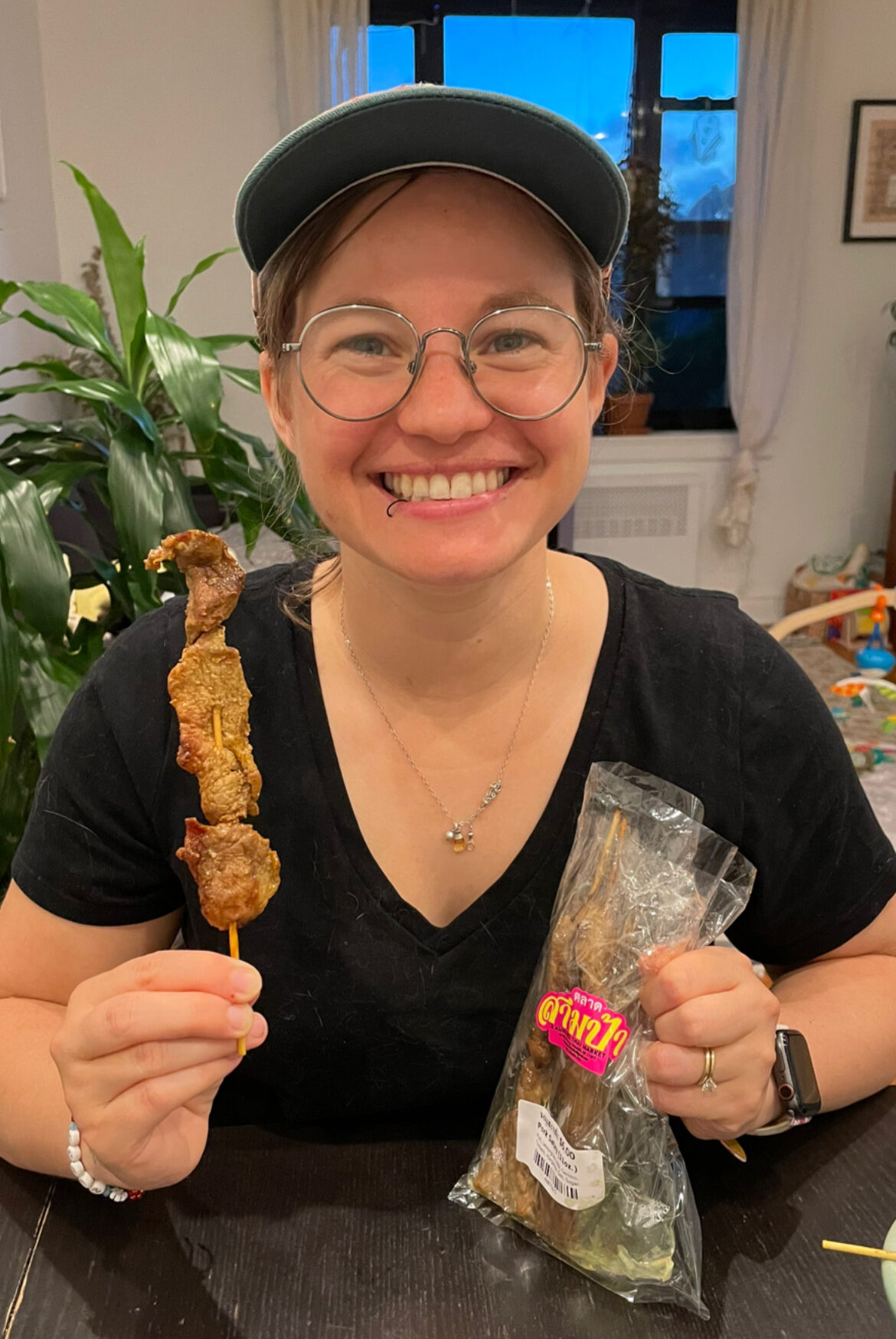 Courtney smiling holding a pork satay skewer from 3 Aunties Thai Market