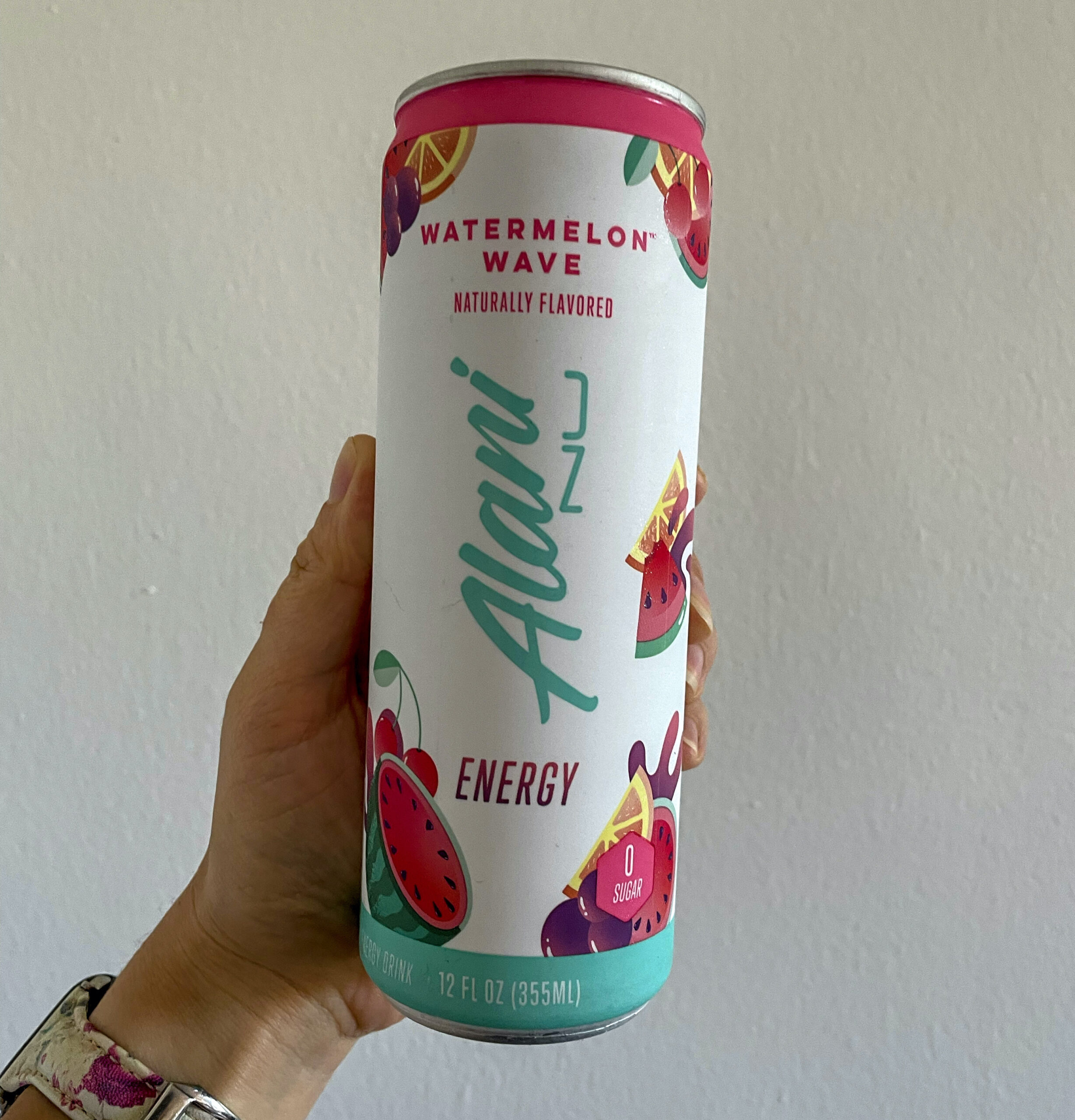 A hand holding a can of Alani Watermelon Seltzer